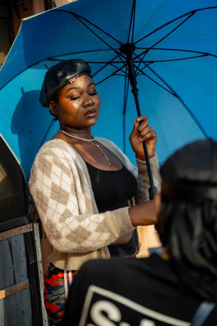 Cast member waiting beneath a blue umbrella during the Nigeria shoot