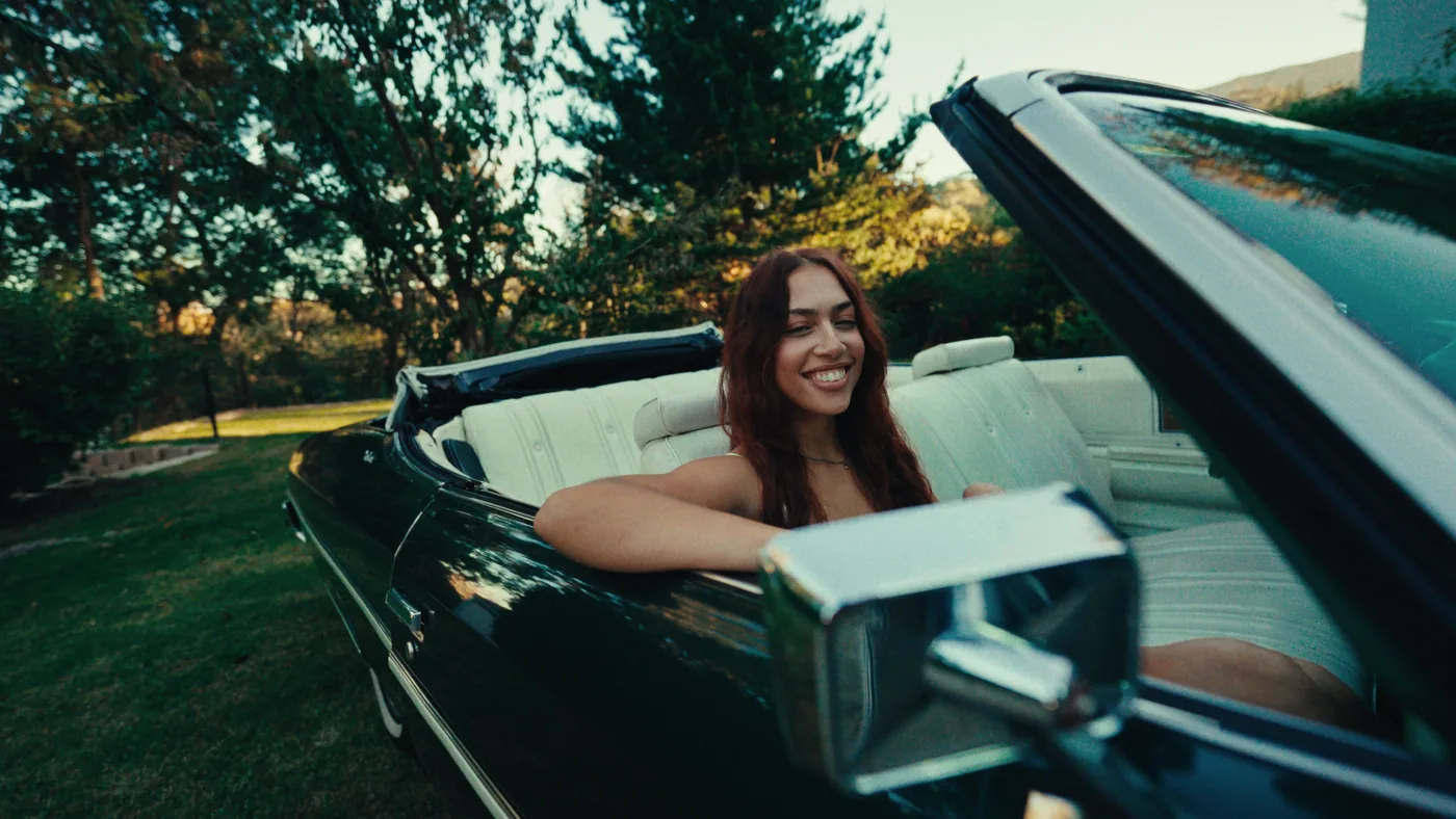 Woman smiling in a black convertible during the OMO video