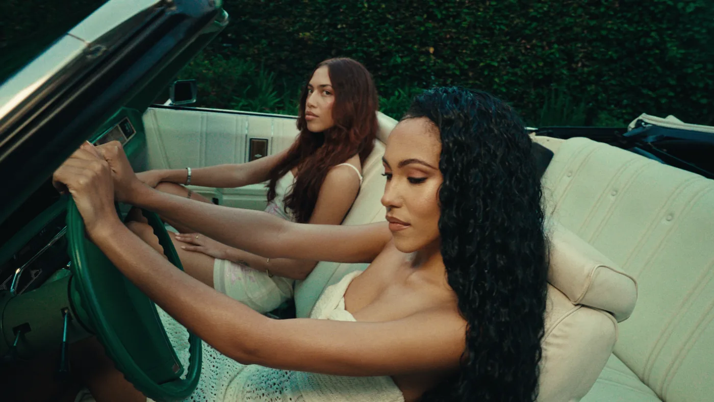 Two women styled in white inside a classic convertible